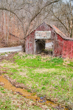 Road and creek next to old faded red barn in midwest with dead forest