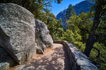 Paved hiking path alongside large boulders with stone wall