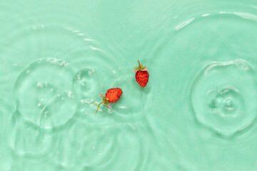 Fresh red woodland strawberries in aquamarine calm water with splashes and waves.