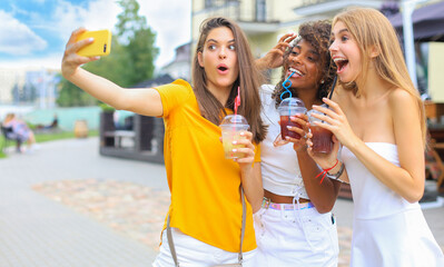 Three trendy cool hipster girls, friends drink cocktail and taking selfie in city background.