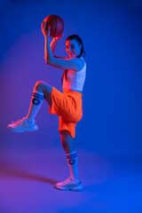 sports girl in the studio in shorts, a T-shirt with a basketball. blue background. sport concept. sport, healthy lifestyle. fuzzy image, blur. colored light