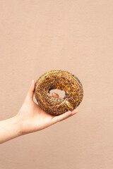 bagel with poppy seeds in hand on a beige background