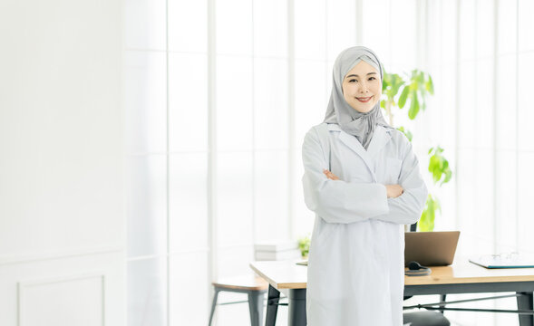 Asian woman in a lab coat wearing a hijab standing in the office.