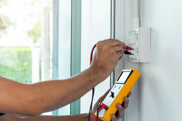 Electrician using a digital meter to measure the voltage at a wall socket on the wall.