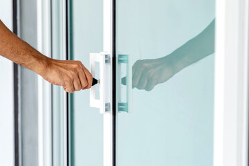 Close-up of man's hand opening a glass door with a key.