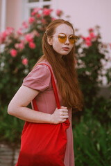Young beautiful red-haired long-haired woman in a summer pink dress walks through the streets of a summer city.