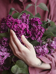 The girl holds a bouquet of lilacs on the background of a pink shirt. Spring concept