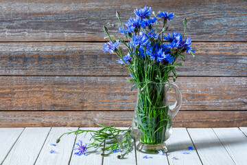 Bouquet of blue cornflower flowers in a glass vase on a wooden table