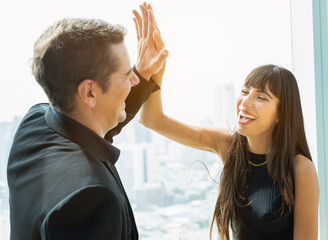 woman happy greeting and high five with man, businesswoman claps businessman in relax workplace with window background. colleague team working in modern office