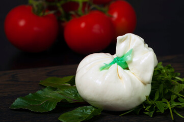 Italian mozzarella cheese and cream burrata on a black slate board with arugula and spinach greens with red tomatoes on a black background.