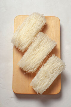 skeins of raw Korean starch noodles tanmen lie next to each other on a wooden board on a gray background, close-up, top view.