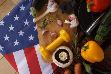 Gym dumbbells, vegetables, sausages and flag of the United States of America. Fit barbecue party...