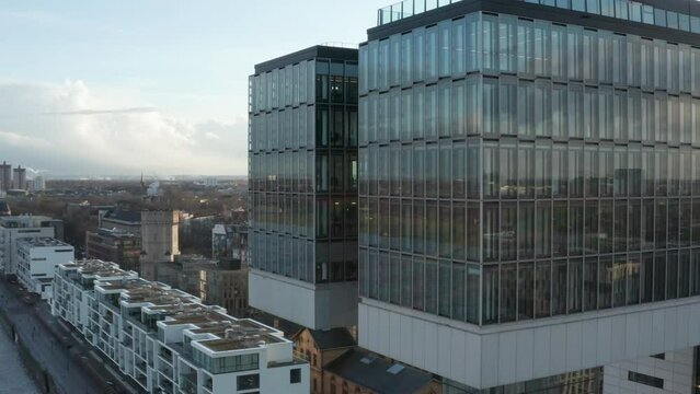 Slide and pan footage of building with glass facade standing on waterfront. Reflection of surroundings and sunshine. Cologne, Germany