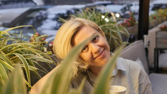 Portrait: A happy Caucasian attractive blonde smiles a beautiful smile with dimples on her cheeks, sits at a table in a summer restaurant and is lit by the warm light of a lamp.