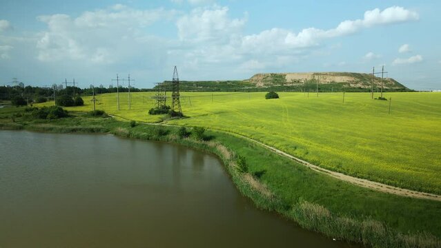 Blooming rapeseed field. On the edge of the field there is a pond. A mothballed city dump is visible on the horizon. Aerial photography.