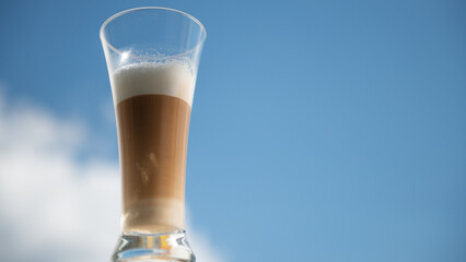 multilayer coffee or cappuccino in a glass against the blue sky