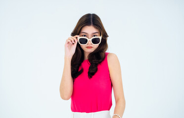 Portrait of a stylish cool beautiful young Asian woman dressed in pink sleeveless summer clothes touching sunglasses and looking at camera isolated on white background.