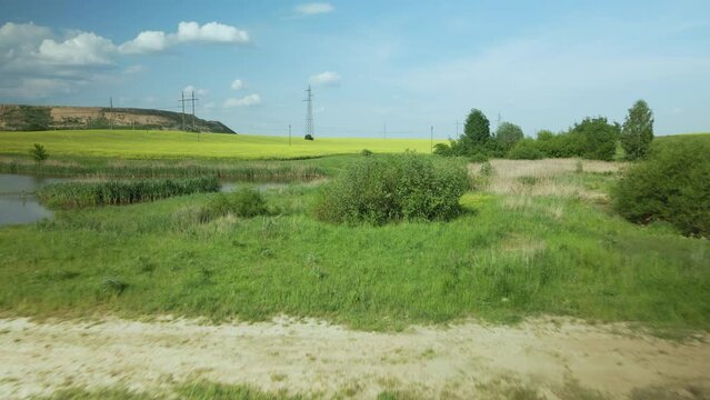 Blooming rapeseed field. On the edge of the field there is a pond. A mothballed city dump is visible on the horizon. Aerial photography.