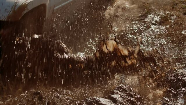 Utility vehicle drivings mud pit obstacle spreading splashes to sides on race on off road, closeup. SUV drives through dirty road