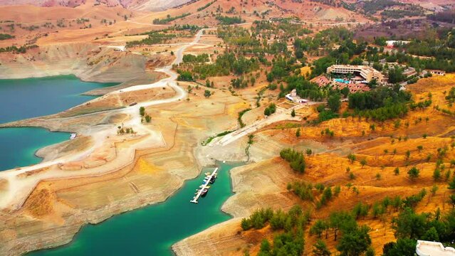 Aerial Shot Of Outdoor Swimming Pool By Hotel On Hill, Drone Flying Forward Over Nautical Vessels Moored In Lake - Kurdistan, Iraq
