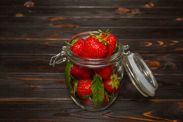 Fresh strawberries in a glass jar stands on a wooden background