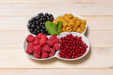 Bowl with natural ripe organic berries with peduncles on wooden table, top view with copy space