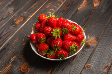 A bunch of fresh strawberries in a ceramic bowl on a rustic wooden background.