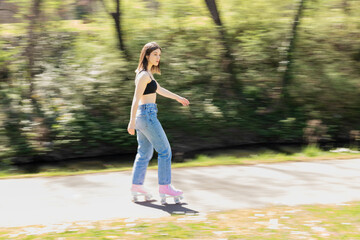 brunette woman skating in a park with pink roller skates