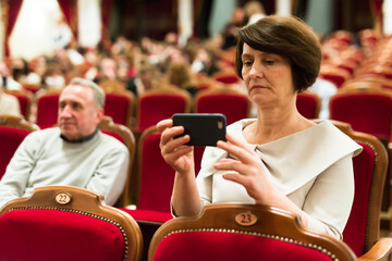 woman takes picture of performance with his phone in theater hall