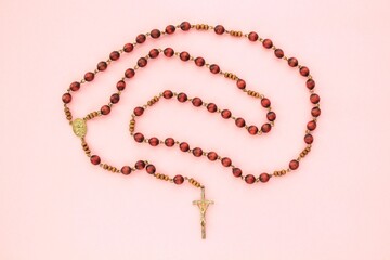 Rosary wooden beads and crucifix christian cross on holy bible book on pink background. Catholic symbol. Flatlay, top view. Pray for God, faith in Jesus Christ and believe religion concept. Closeup