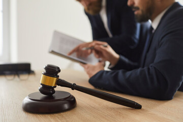 Close up of judge gavel standing on sound block on table against background of judge and lawyer....