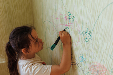Top view of little spoilt girl with dark hair wear T-shirt, holding green marker in hand, drawing...
