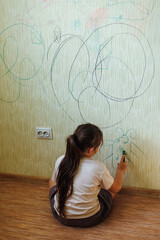 Back view of little naughty girl with dark hair wearing T-shirt, holding green marker in hand,...