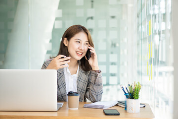 Fototapeta na wymiar Portrait of Asian businesswoman talking on smartphone writing on laptop computer in home office Startup business sme telemarketing beautiful woman working in modern office