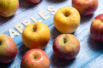 Many yellow and red apples fruit with apples word written on wooden letters on a blue background