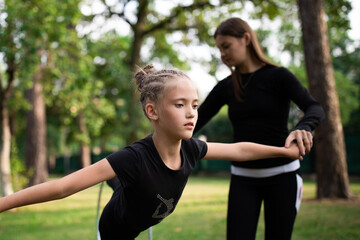 Coach teaching her trainee to work with hoop on rhythmic gymnastics training outdoors in summer in sports camp