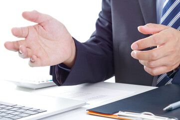 Obraz premium パソコンの前で手振りで話すスーツ姿の男性