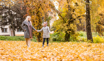 Fototapeta premium Mother and daughter having fun in the autumn park among the falling leaves.