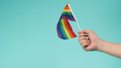 LGBT concept.Hand is holding a rainbow flag on mint green or tiffany blue background.