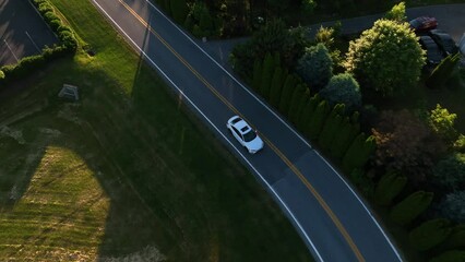 Tracking shot of Honda Civic driving through residential neighborhood. Midsize sedan travel through rural farmland. Suburbia with sunflare at sunset.