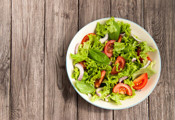 Salad with tomatoes, basil, arugula and onions. Summer salad with tomatoes and herbs on wood background