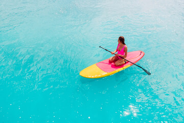 Attractive woman in pink swimwear floating on stand up paddle board on a quiet ocean. SUP surfing...