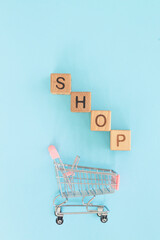 Small metal cart and word shop on blue background. Shopping concept