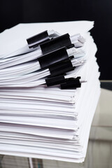 A stack of office papers, some of which are fastened with black binders