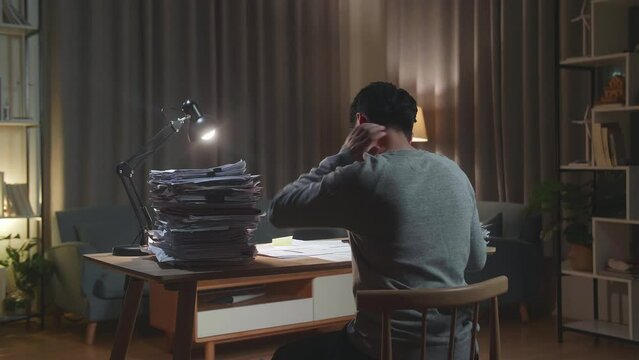 Back View Of Asian Man Having Neck Pain While Working Hard With Documents At Home
