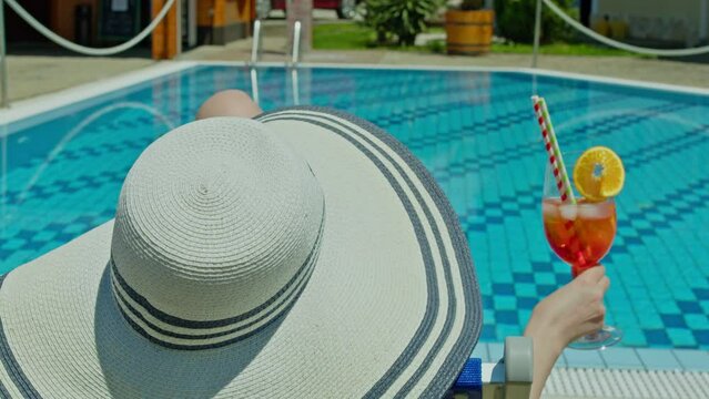 Woman relaxing at poolside in summer drinking cocktail. Aperol spritz is the perfect cold and refreshing drink on summer vacation. Slow motion 4k video.