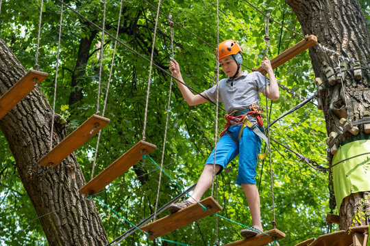 Rope park. A boy teenager in a helmet walks on suspended rope ladders. Carabiners and safety straps. Safety. Summer activity. Sport. Children's playground in nature in the forest.