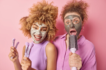 Two curly haired European women friends apply beauty masks undergo skin care and cosmetic...