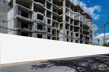 Empty long hoarding with white mockup space on construction site against grey wall of unfinished...