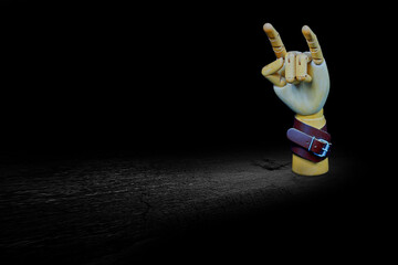 Wooden articulated hand with leather strap makes the Sign of Horn/ Heavy Metal symbol in front of a black background